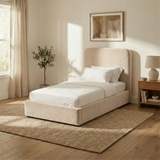 Angled view of beige velvet single ottoman bed showing upholstered frame, curved headboard, and low base design