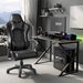 Ergonomic gaming chair with lumbar support and padded armrest in black leather finish, placed beside a modern gaming desk setup in a home office.