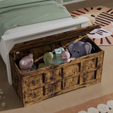 Storage Chest - Shaker Style Blanket or Toy Box With Lid & Safety Hinges in rustic wood finish, placed at the foot of a bed and filled with plush toys.