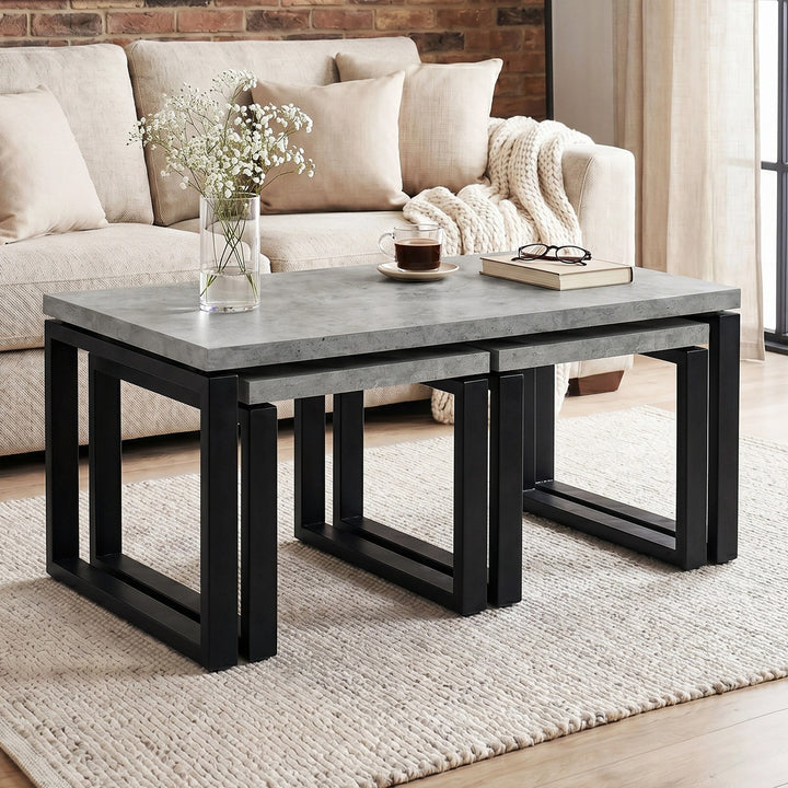 [Concrete] Nestline nesting table view showing in a bright lounge with cream sofa, brick wall, vase stems, and nested frames