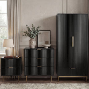 [Black] flutrina black 2 door wardrobe, 3 drawer chest and 2 drawer bedside grouped on brass legs against a panelled wall