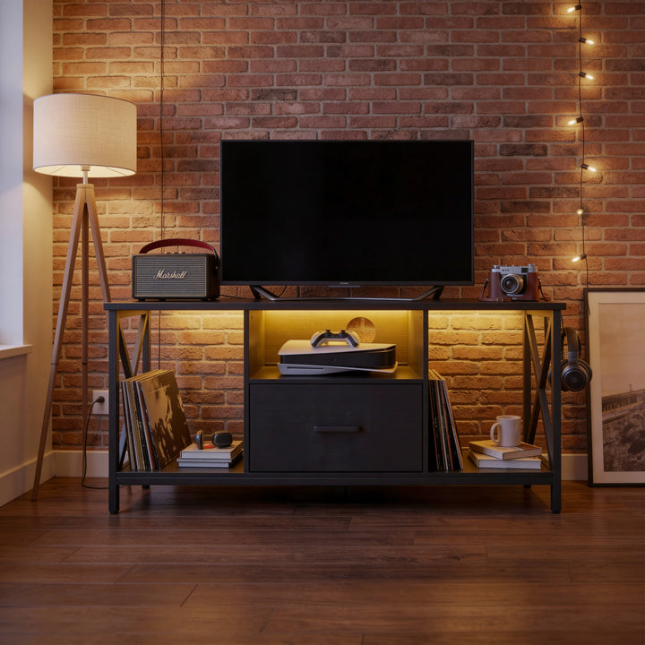 [Black] Calvera TV unit in industrial brick-wall living room, amber LED glow under the TV and books in side cubby