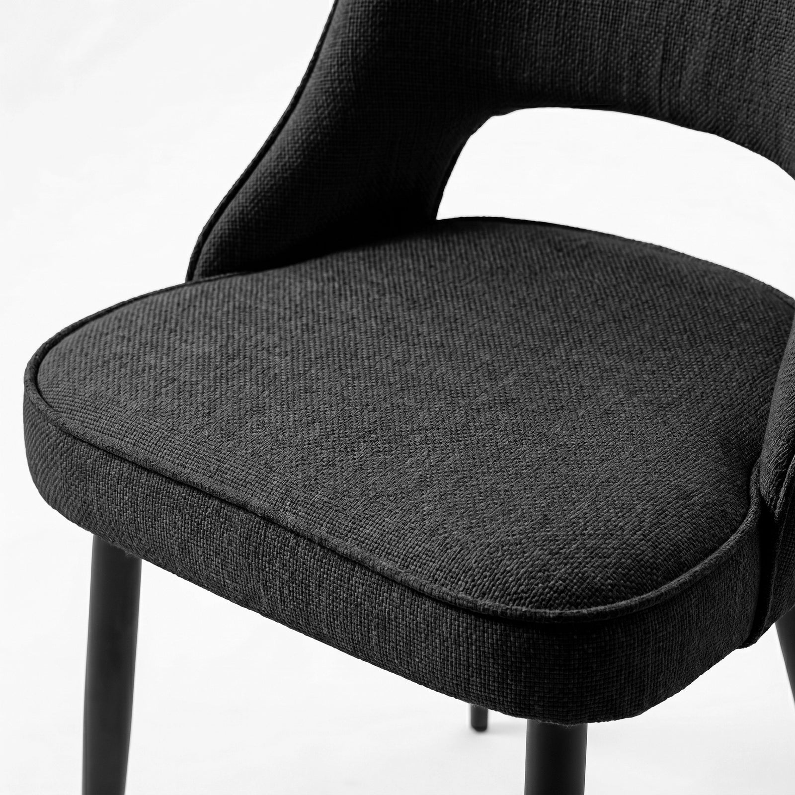 [Black | Set of 2] Comfy dining chair close-up of fabric seat, piped edge, curved open back and black metal legs.
