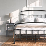 [Black | Double] Close view of the black curved front rail, vertical bars and white bedding beside a small table.