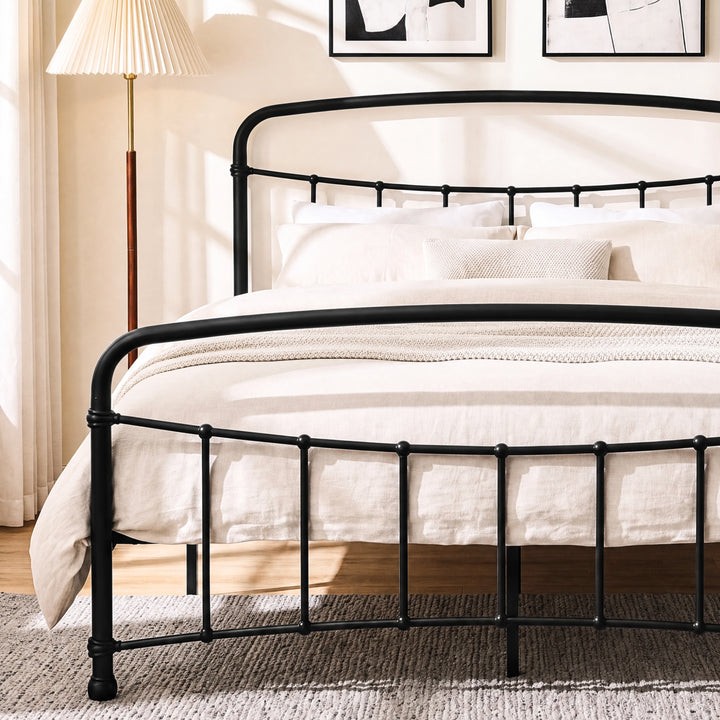 [Black | King] Close view of the black curved front rail, vertical bars and cream bedding beside a wooden table.