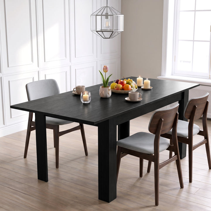 [Black Wood] Closed black wood-effect dining table styled with fruit, flowers and candles; three chairs stand around its legs.