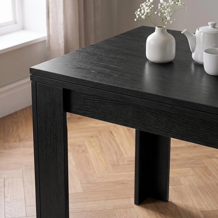 [Black] Close-up of the folded wood-grain tabletop above apron and wide legs, with white flower vase, teapot and cup
