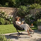 [Black] Woman reading a book in a hanging egg chair in a garden setting