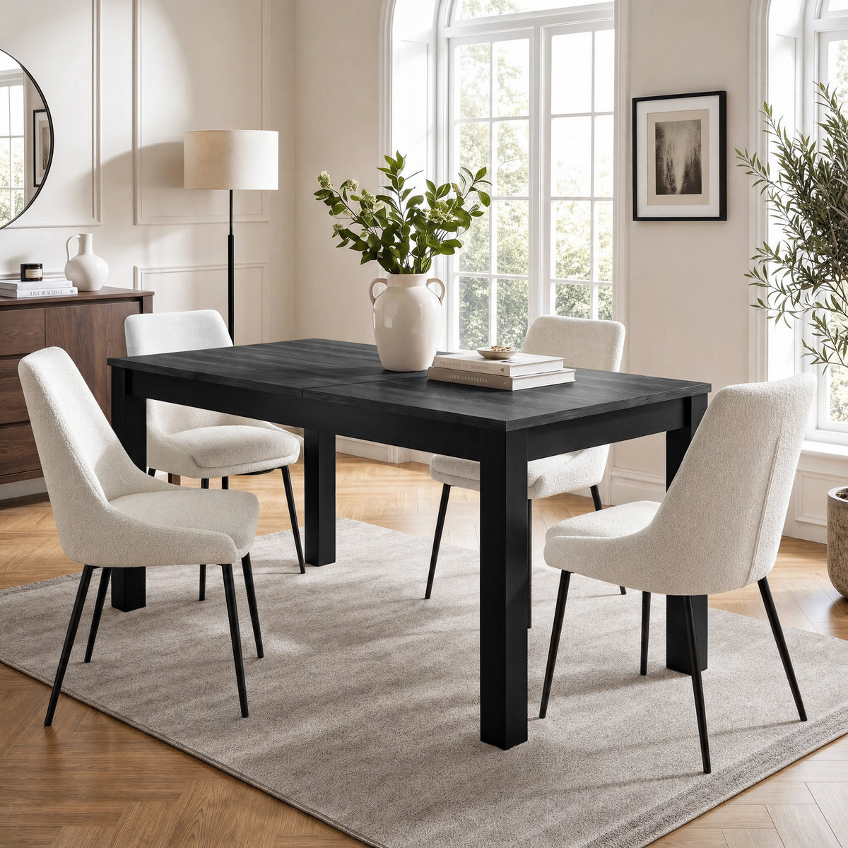 [140cm | Black] Closed table in bright dining room with four cream chairs, vase, stacked books, rug, and window light