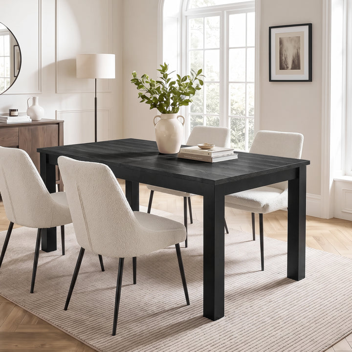 [160 cm | Black] Closed 160cm extendable dining table with four cream chairs, leafy vase and books in a bright dining room.