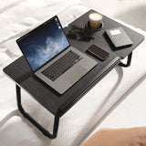 black laptop table placed on a bed with a phone, tea cup, and computer accessories neatly arranged