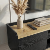 [Black | 112 cm] Larvik close-up of oak top surface with pampas grass vase, remote control, stacked books, and black woodgrain side panel