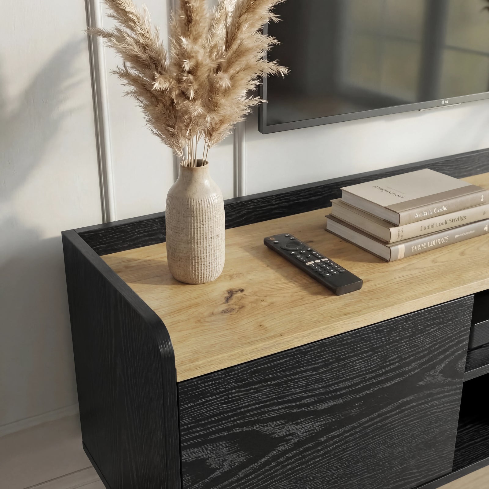 [Black | 112 cm] Larvik close-up of oak top surface with pampas grass vase, remote control, stacked books, and black woodgrain side panel