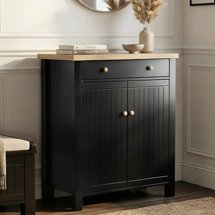 [Black] Linra shoe cabinet front view with oak top, top drawer, grooved double doors, and oak knobs beside a hallway bench