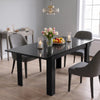 [Black Marble] Closed glossy dining table styled with fruit, flowers, and candles; grey chairs stand around its thick legs.