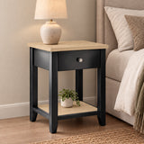 [Black] Angled view of Black Shaker Bedside Table with natural oak top, drawer, and open shelf styled by bed.