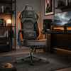 [Black + Orange] gaming chair with the Xstriker logo on the headrest, backrest, and lumbar support, positioned in a modern, dimly lit home office setup.