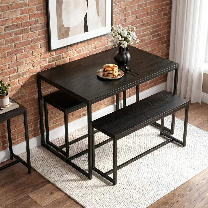 [Black] Orvak dining table and two benches in a compact industrial brick-wall setting, styled with pancakes and a white flower vase centrepiece