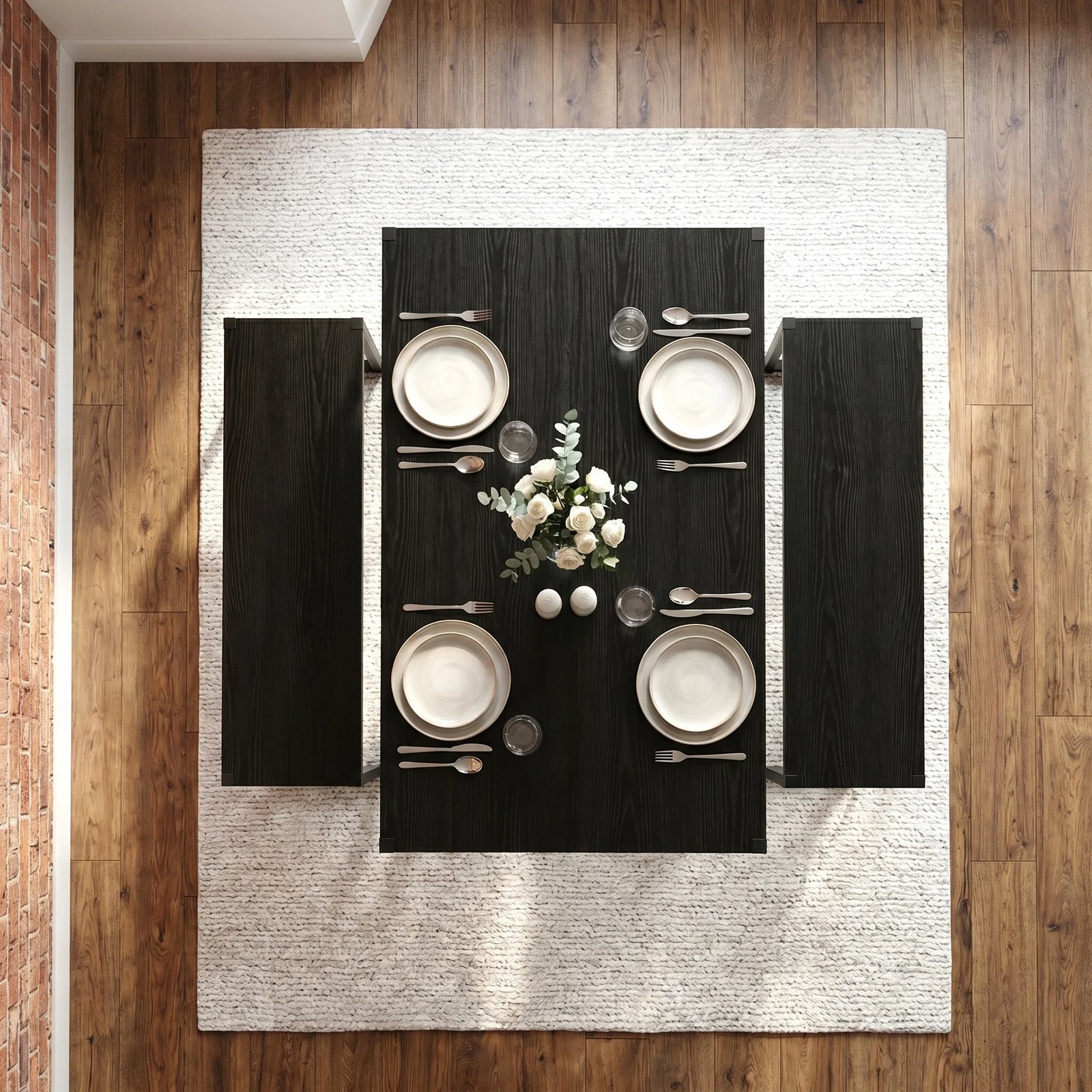 [Black] Orvak dining table seen from directly above with two benches, four place settings, cutlery, glassware, and a white rose centrepiece