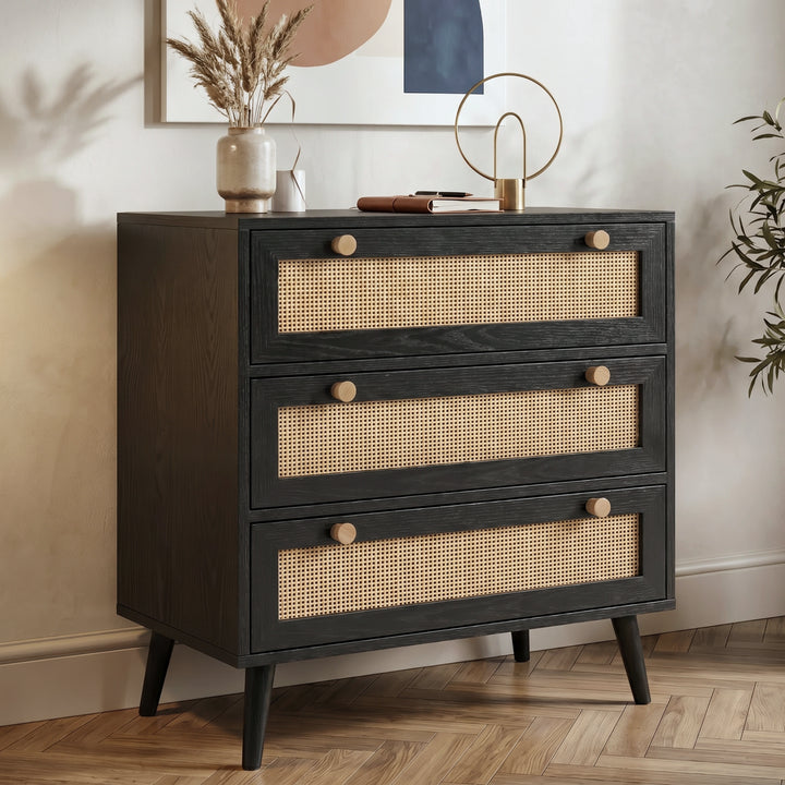 [Black] Rattan chest of drawers angled view showing three rattan-front drawers with wooden knobs on herringbone floor