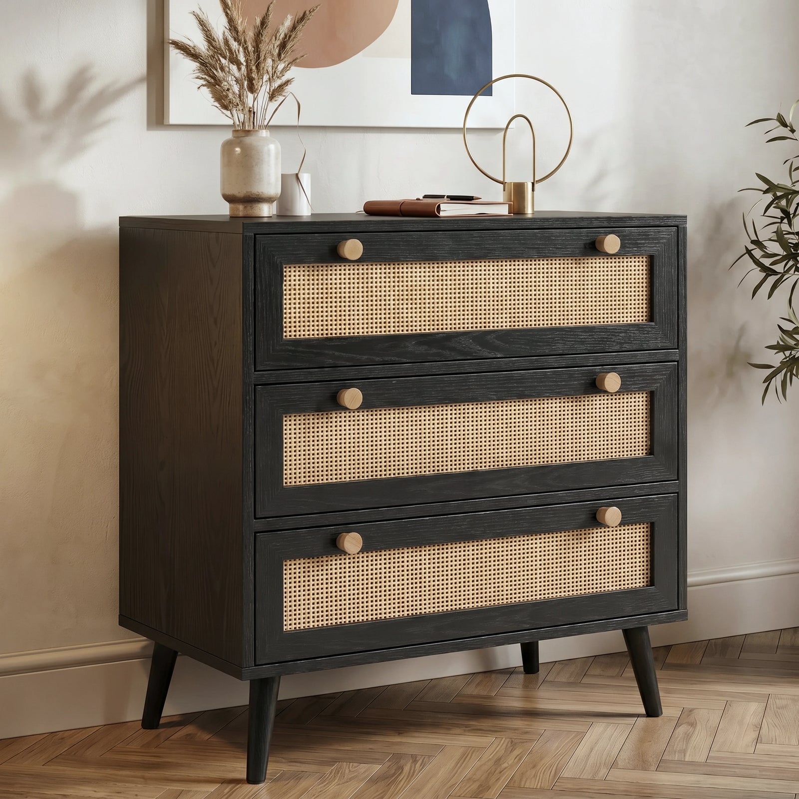 [Black] Rattan chest of drawers angled view showing three rattan-front drawers with wooden knobs on herringbone floor