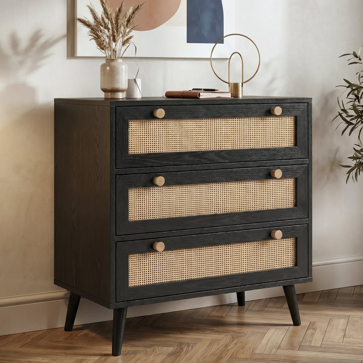 [Black] Rattan chest of drawers angled view showing three rattan-front drawers with wooden knobs on herringbone floor
