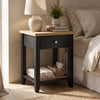 [Black] Angled view of Black Shaker Bedside Table with natural oak top, drawer, and open shelf styled by bed.