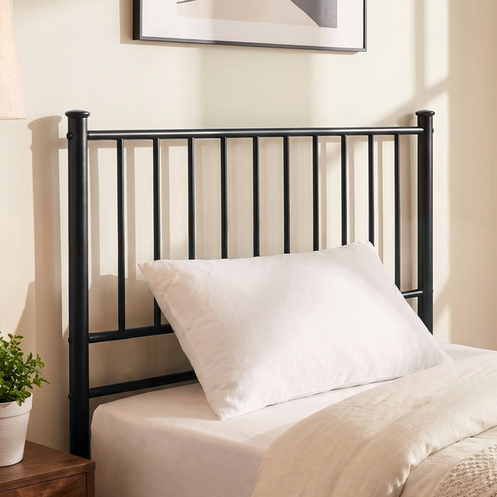 [Black | Single] Metal bed foot-end view with bar headboard and footboard, cream-white bedding, centre leg, lamp and plant.