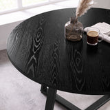 [Black Wood] Close-up of the round wood-effect tabletop with bold grain patterns, styled with a vase, cup and newspaper.