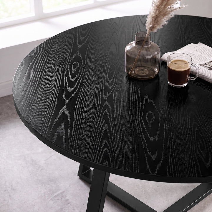 [Black Wood] Close-up of the round wood-effect tabletop with bold grain patterns, styled with a vase, cup and newspaper.