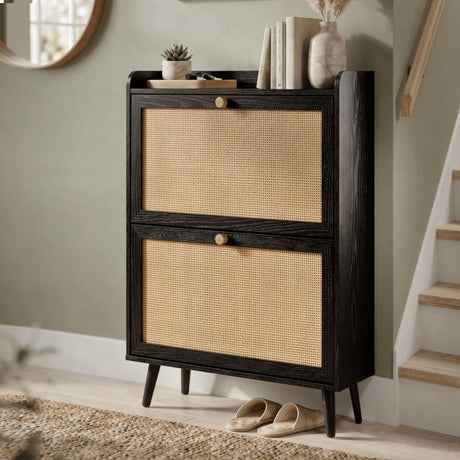 [Black] Wovena shoe cabinet three-quarter angle view with closed rattan panel drawers, mid-century tapered legs, and top shelf styled with books and vase