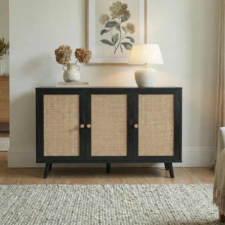 [Black] Wovena 3-door sideboard against a neutral wall below a botanical print, styled with dried hydrangeas in a white vase, stacked books, and a ceramic table lamp