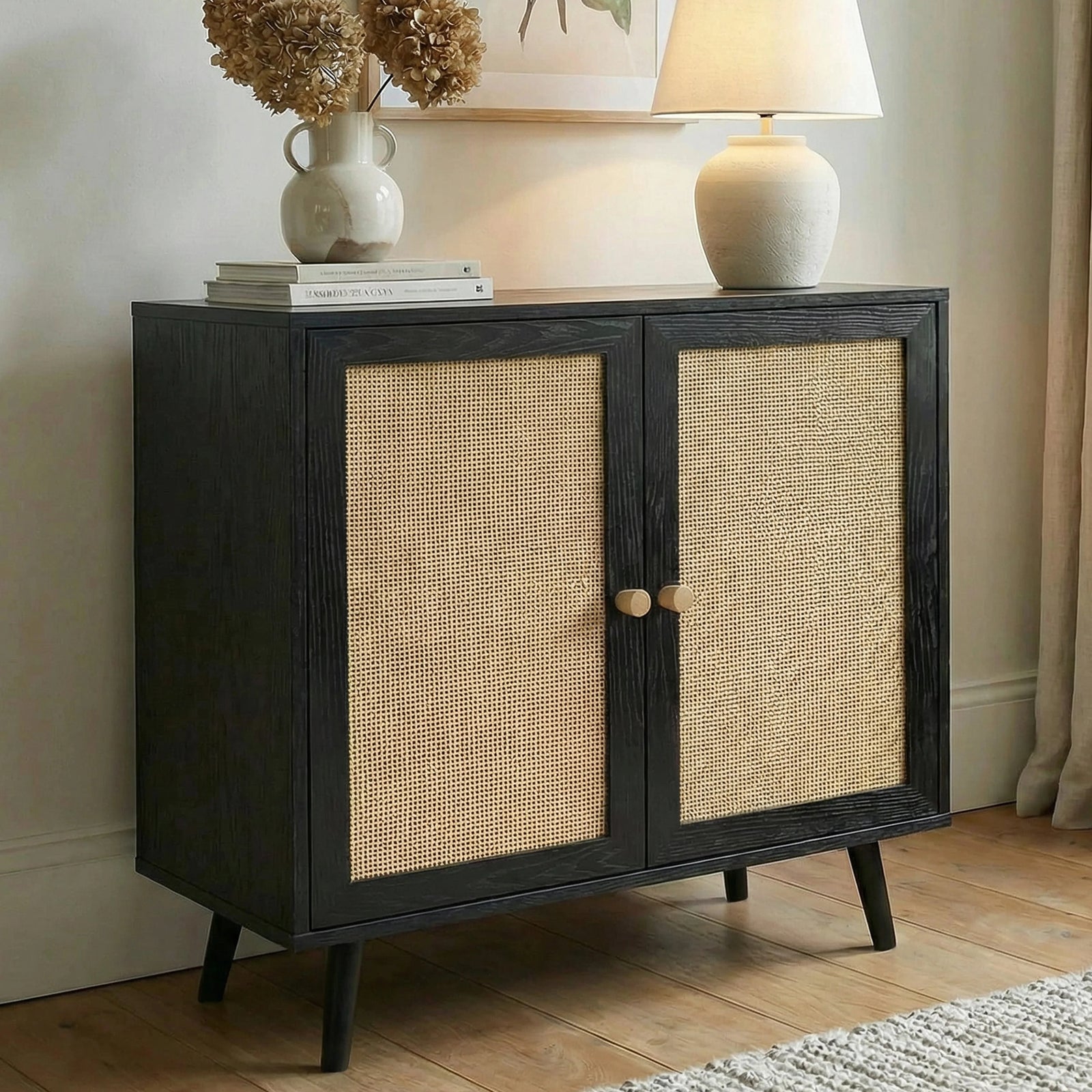 [Black] Wovena rattan sideboard styled with a ceramic vase of dried stems and a white lamp on top against a neutral wall