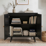 [Black] Rattan sideboard with both doors open revealing two storage shelves filled with books and accessories