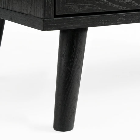 [Black] Wovena close-up of a solid tapered black-stained leg showing natural wood grain through the dark finish where it meets the ebonised cabinet base corner