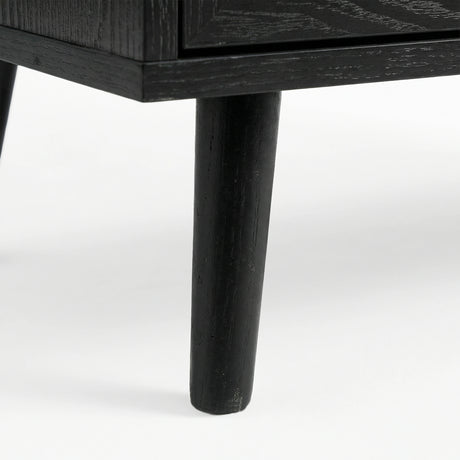 [Black] Wovena close-up of a solid tapered black-stained leg showing natural wood grain through the dark finish where it meets the ebonised cabinet base