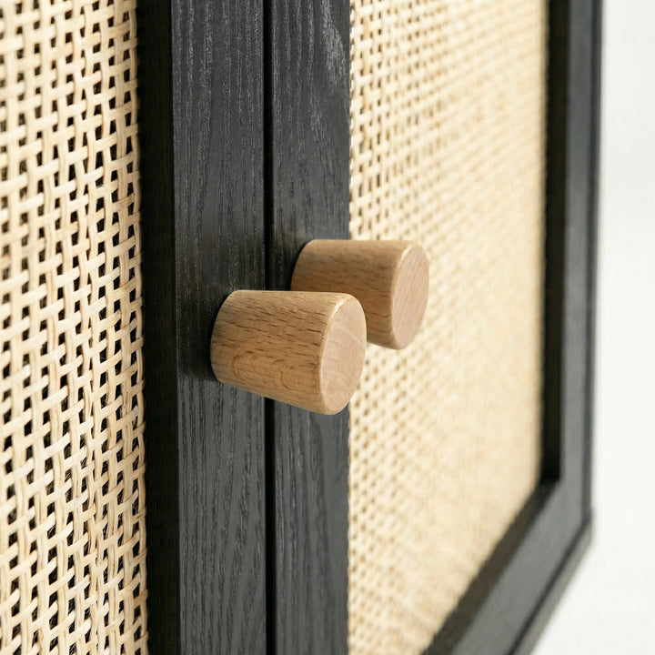 [Black] close-up of two cylindrical oak knobs paired on the centre stile between woven rattan door panels