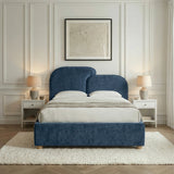 Front-facing view of a blue double bed with padded headboard, centered between bedside tables and warm lamps