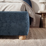 [Double | Blue] Lower corner of a blue fabric bed frame with rounded edges and small wooden legs placed on wooden flooring