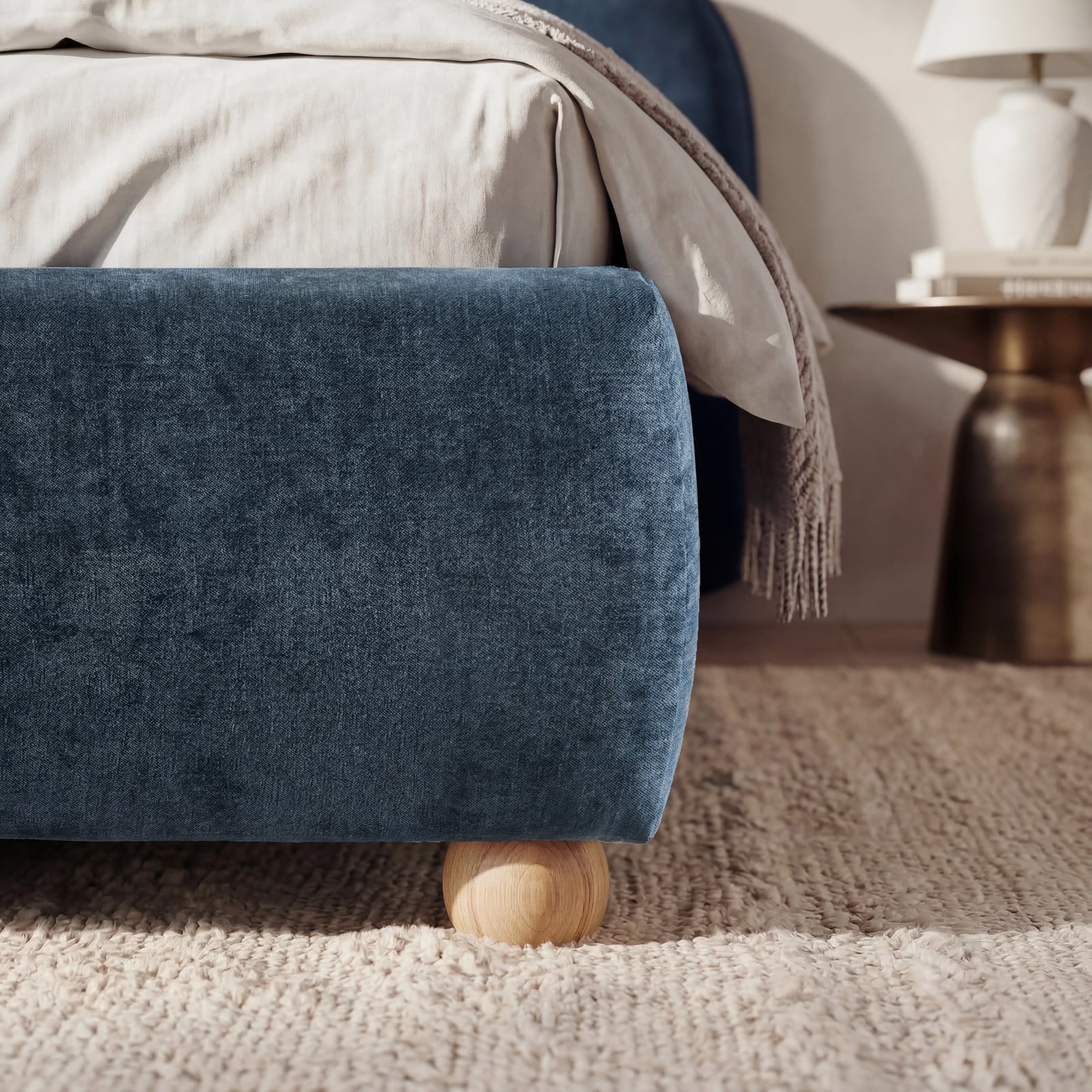 [Double | Blue] Lower corner of a blue fabric bed frame with rounded edges and small wooden legs placed on wooden flooring