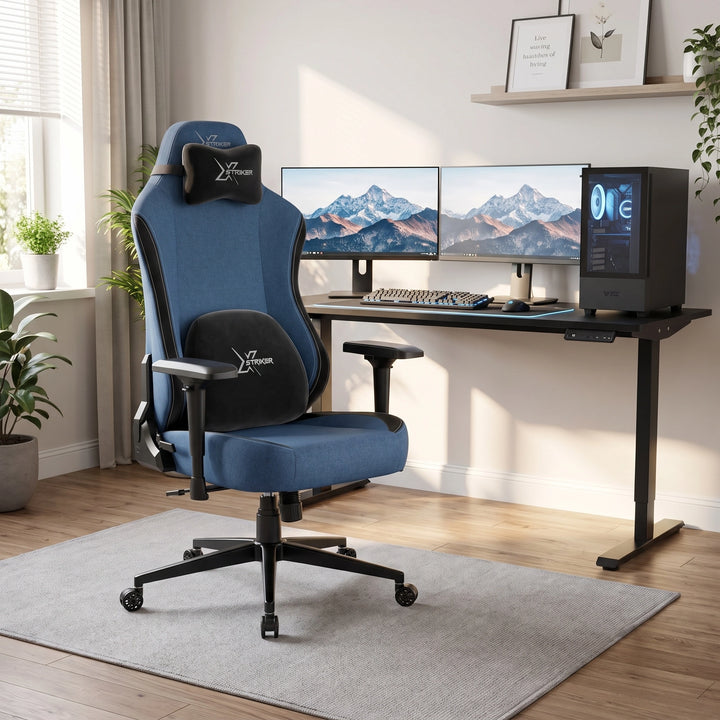 [Blue] ergonomic gaming office chair with black accents and a headrest pillow, positioned in front of a black computer desk setup with dual monitors in a bright home office
