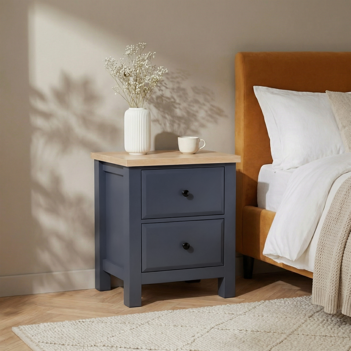 [Blue] Haven bedside table in bedroom corner next to mustard headboard with vase and mug on oak top