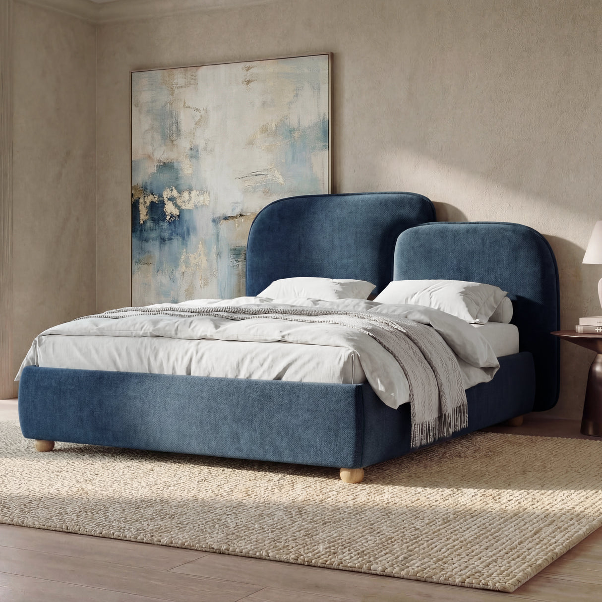 [King | Blue] Angled view of a upholstered bed positioned near a window with neutral bedding and matching bedside tables