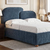 [King | Blue] upholstered bed frame with a tall curved headboard and matching footboard, shown in a styled bedroom setting with white bedding, bedside tables, lamps, and a rug.