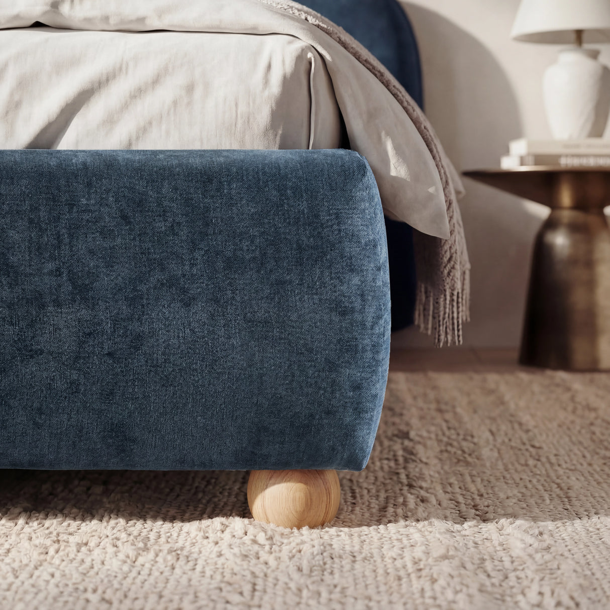 [King | Blue] Lower corner of a blue fabric bed frame with rounded edges and small wooden legs placed on wooden flooring