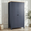 [Blue] Linra 2 Door Wardrobe in a white panelled room with woven basket and throw beside it, showing grooved door fronts and oak top