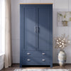 [Blue] wooden two-door wardrobe with a light natural wood top and silver handles, set in a styled room with a window, curtain, wall art, and a vase of flowers.