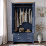 [Blue] wardrobe with a light wood top, shown open in a styled room. Inside, multiple garments hang on a rod, and a handbag and hat rest on a shelf.