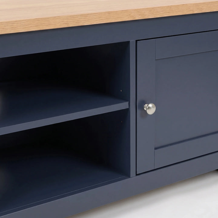 [Blue] Close-up of a tv unit with a light oak wood top, featuring a single cabinet door with a silver round knob and open shelving on the left.
