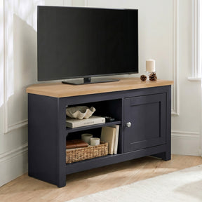 [Blue] Tavero Blue Corner TV Unit with Storage three-quarter view against white panelled wall showing oak top, open shelving with wicker basket and shaker door